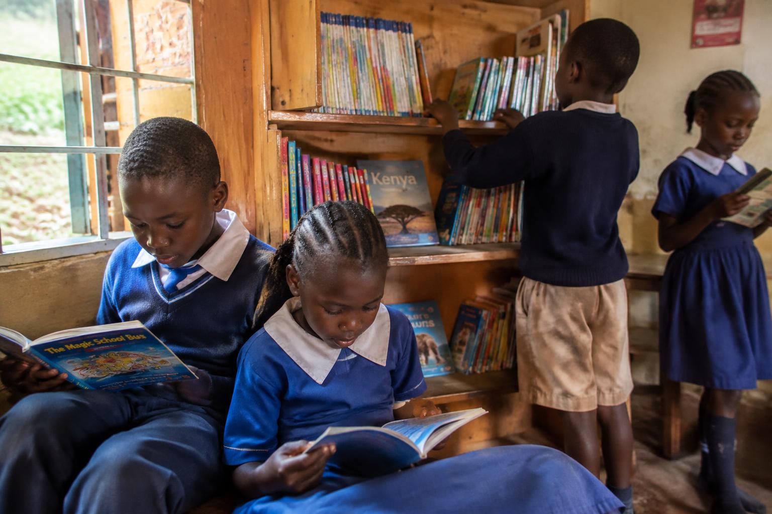 Kenyan schoolchildren reading beside a wooden bookshelf in a classroom corner